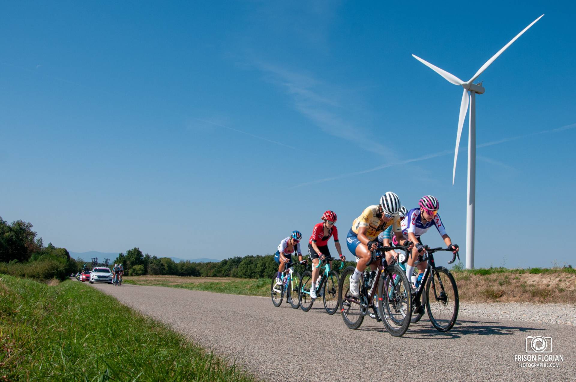 Une échappée du Tour Cycliste Féminin International de l'Ardèche 2023 devant un éolienne.